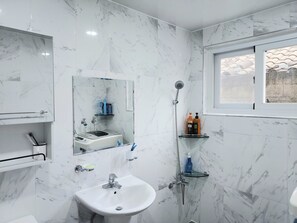 Un baño moderno con pared de mármol, un lavabo, un espejo, una ducha y una ventana.