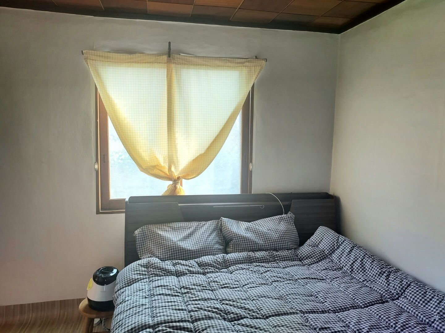 A bedroom with a bed, a window with a sheer curtain, and a bedside table with a lamp.