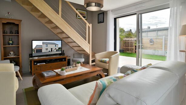 A living room with a sofa, armchair, coffee table, TV, wooden staircase, and a view of the backyard. - La Halte Cancalaise (Cancale)