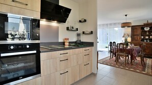 A modern kitchen with wooden cabinets, a built-in oven, and a flat-screen TV. - La Halte Cancalaise (Cancale)