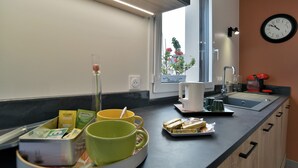A modern kitchen with a black countertop, a coffee maker, a sink, and a window with a view of flowers. - La Halte Cancalaise (Cancale)