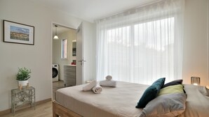 A bedroom with a bed, pillows, a potted plant, a washing machine, and a mirror in the background. - La Halte Cancalaise (Cancale)
