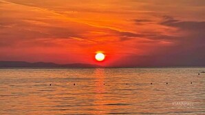 Un coucher de soleil sur une étendue d’eau calme, avec un horizon bien visible et des reliefs terrestres au loin.