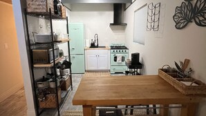 Una cuina compacta amb una taula de fusta, una placa de cocció integrada i una prestatgeria metàl·lica.