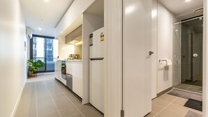 A modern kitchen with a refrigerator, oven, and sink. There is a glass door leading to a shower area. - Cosy Apartment in the heart of Melbourne + Free Wi-Fi + Free Parking (Melbourne)