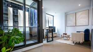 A modern living room with a large sliding glass door, a blue chair, a small table, and a potted plant. - Cosy Apartment in the heart of Melbourne + Free Wi-Fi + Free Parking (Melbourne)
