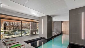 A modern indoor pool area with a glass wall, lounge chairs, and a tiled floor. - Cosy Apartment in the heart of Melbourne + Free Wi-Fi + Free Parking (Melbourne)