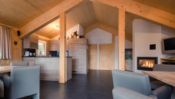 A spacious living area with a high ceiling and exposed wooden beams, a fireplace, and a kitchen area with modern appliances. - #27 mit IR-Sauna und Sprudelbad Innen by Interhome (Turracher Höhe)