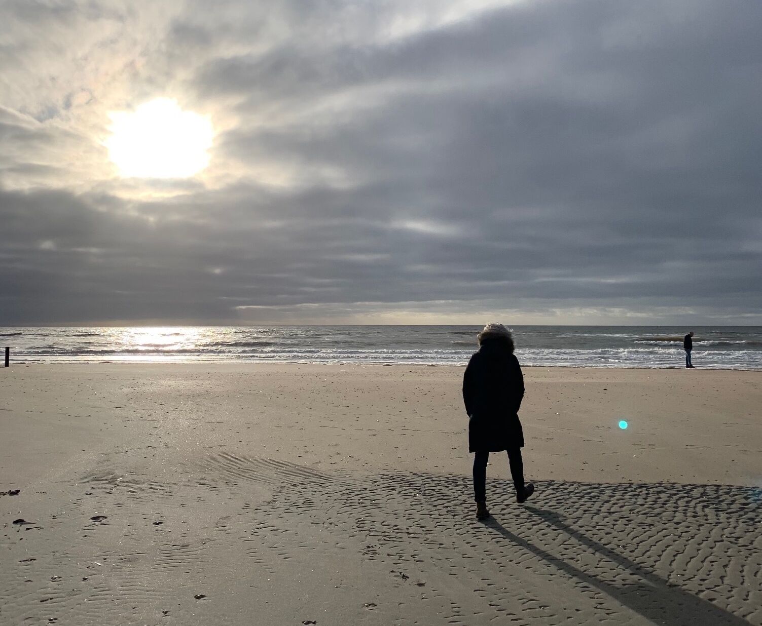 A person walking on a beach with the sun setting in the background.