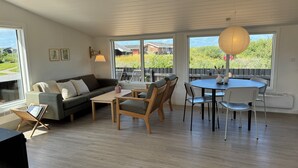 Un vaste espace de vie comprenant un canapé, une table basse et une table à manger avec des chaises. De grandes fenêtres offrent une vue sur l’extérieur.