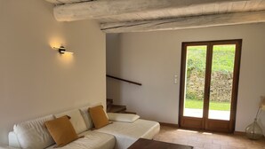 Una sala de estar con un sofá blanco, una mesa de centro de madera y una pared de piedra visible a través de un ventanal.