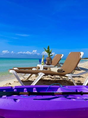 A beach scene with two sun loungers, a small table with a bottle and a plant, and a purple inflatable float in the foreground. - Beachside  Cottage, Sleeps up to 3 (playa del secreto)