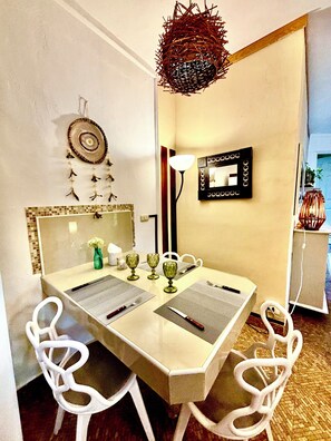 A dining area with a white table, four white chairs, a decorative hanging, a wall-mounted mirror, and a floor lamp. - Beachside  Cottage, Sleeps up to 3, Wi-Fi, Staff, Chef, housekeeping, kayaks (playa del secreto)
