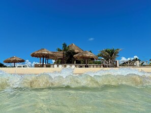 A beachside resort with thatched-roof structures, white lounge chairs, and a clear view of the ocean. - Beachside  Cottage, Sleeps up to 3, Wi-Fi, Staff, Chef, housekeeping, kayaks (playa del secreto)