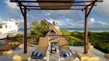 Relax in a tranquil outdoor space with lounge chairs and a shaded pergola, surrounded by lush greenery and ocean views.
