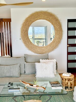 A modern living room with a round woven wall hanging, a glass coffee table, and a view through a large window.