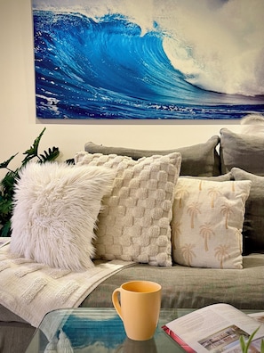 Un salon avec un canapé, une table basse en verre, un livre et un tableau représentant une vague.