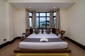 A large bed with a view of a cityscape through a large window, curtains, and a vase of flowers on a bedside table. - Muscatel Yavachi - 400 Mts from MG Marg (Gangtok)