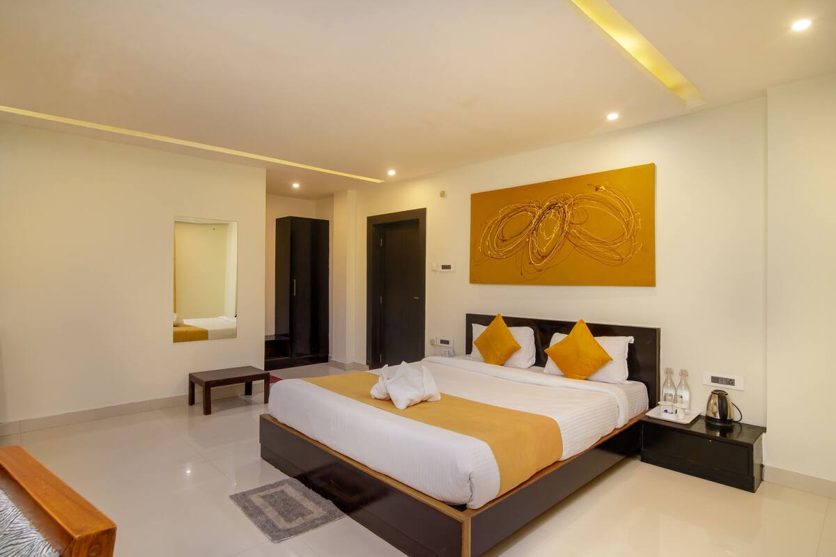 A modern hotel room with a large bed, a bedside table with a lamp, and a wall-mounted artwork.