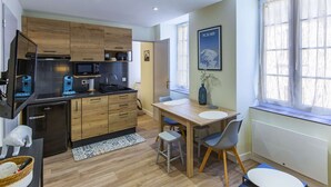 A compact kitchen with modern appliances, a dining area with a table and chairs, and a window with sheer curtains. - Cozy 2-Room Apartment in Cauterets Center - Sleeps 2-4, Well-Equipped Kitchen, Near Ski Lifts (Cauterets)