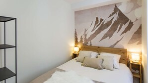 A bedroom with a mountain mural, a wooden headboard, two bedside lamps, and a fluffy white throw blanket. - Cozy 2-Room Apartment in Cauterets Center - Sleeps 2-4, Well-Equipped Kitchen, Near Ski Lifts (Cauterets)