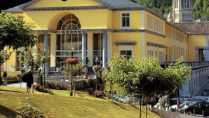 A yellow building with a large arched entrance and a church steeple in the background. - Cozy 2-Room Apartment in Cauterets Center - Sleeps 2-4, Well-Equipped Kitchen, Near Ski Lifts (Cauterets)