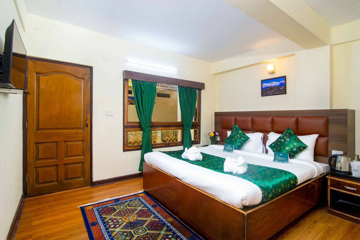 Una habitación de hotel con una cama de madera, cortinas verdes, una mesita de noche y vistas de la ciudad.