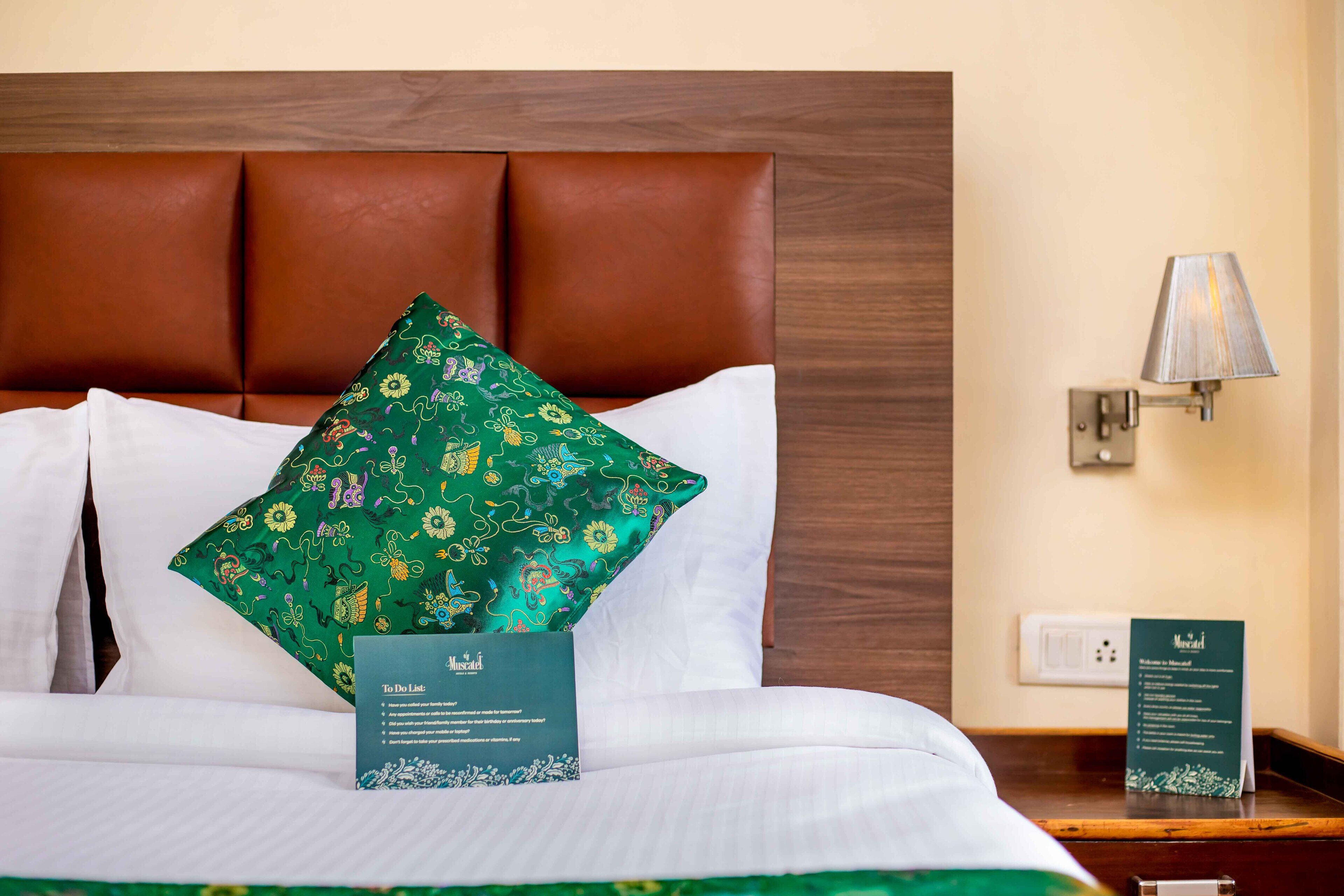 A neatly made bed with a green floral pillow, a white pillow, and a sign on the nightstand.
