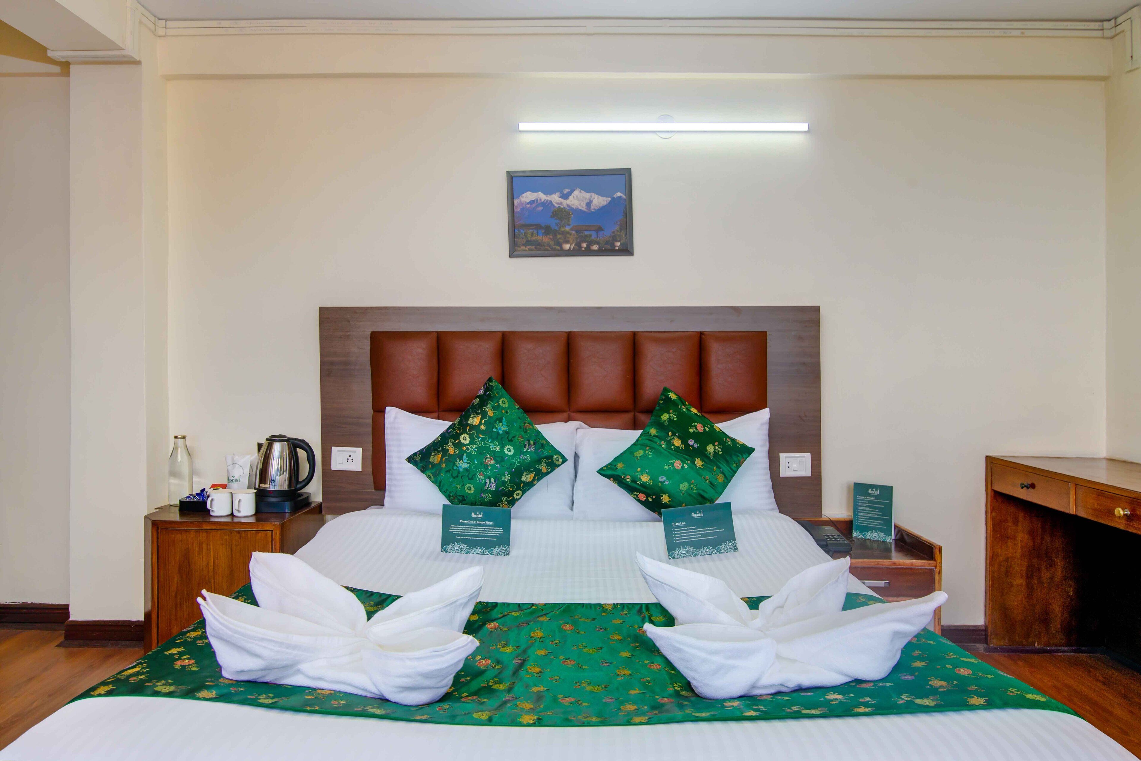 A neatly made bed with green floral bedding, two pillows, and two towels arranged on the bed.