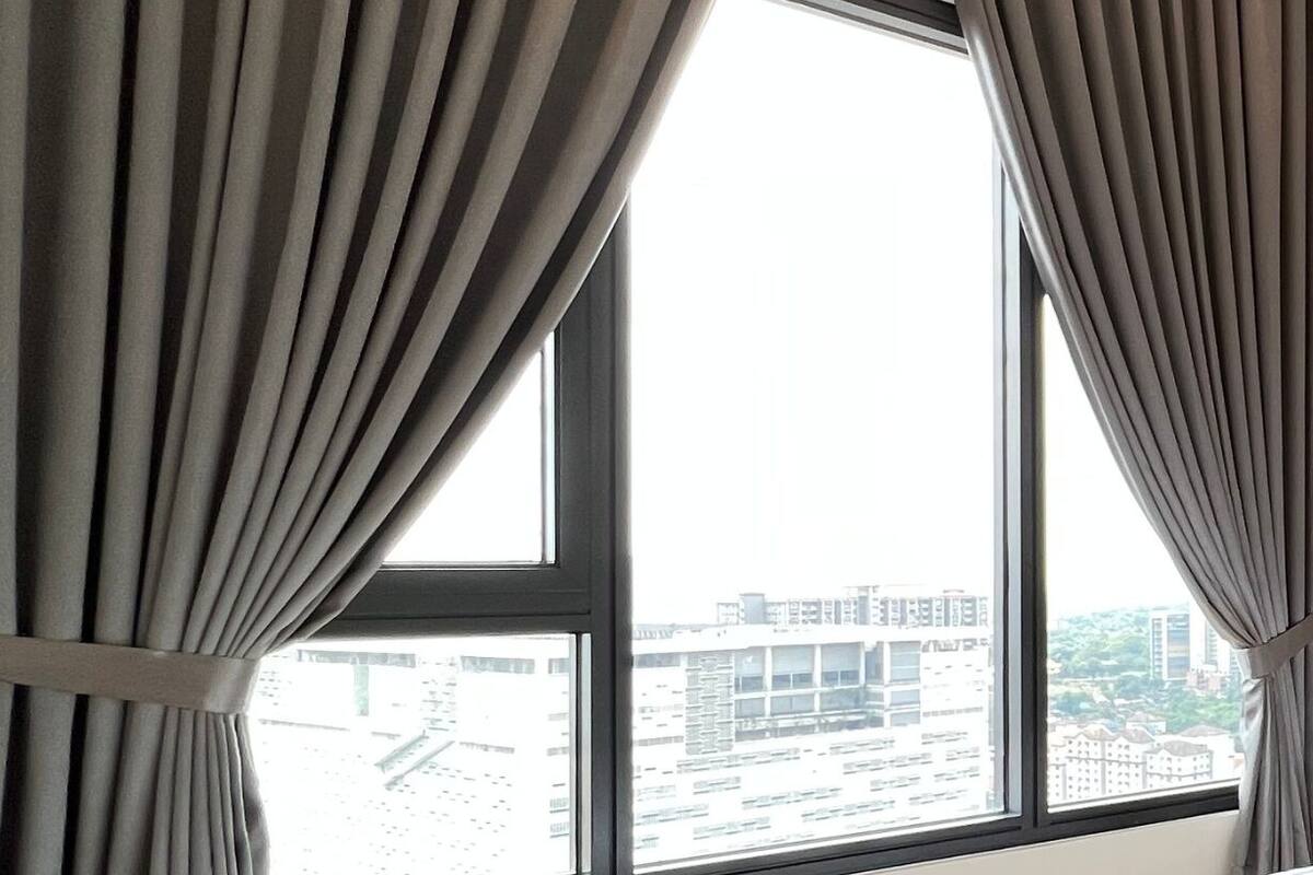 A bedroom with a large window, curtains, a bed, and a view of buildings outside.