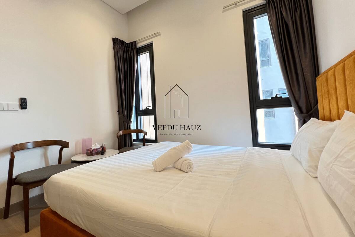 A hotel room with a bed, a chair, a desk, and a window with curtains.