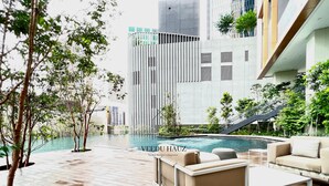 Un espace piscine extérieur moderne, doté d’une terrasse en bois, de mobilier de salon et offrant une vue sur les immeubles de grande hauteur.