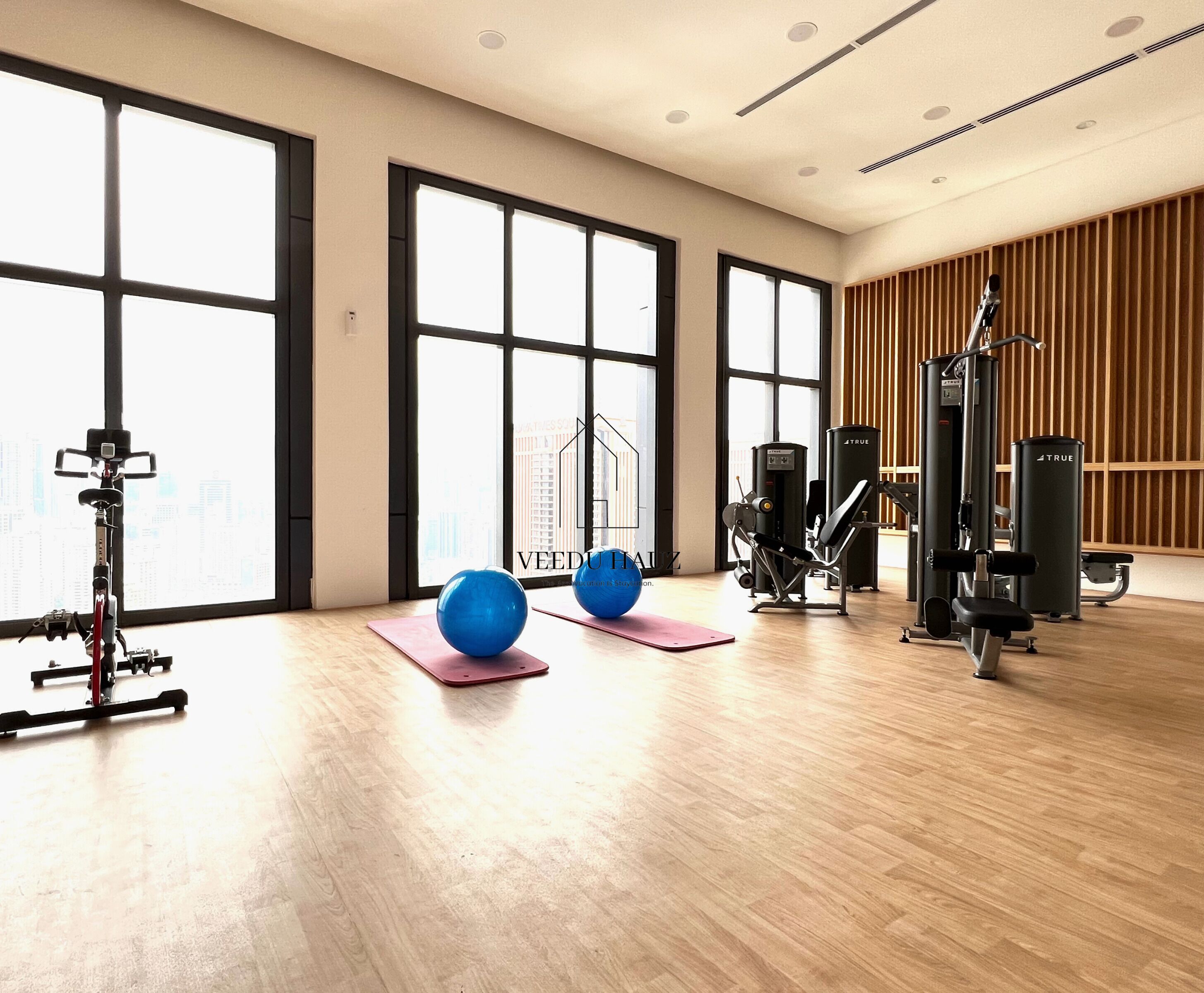 Une salle de sport spacieuse, dotée de grandes fenêtres, de ballons d’exercice et de divers équipements de remise en forme.