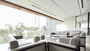 Un salon moderne avec un ensemble canapé et une table basse, de grandes fenêtres offrant une vue sur la ville et un balcon doté d’une balustrade.