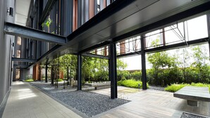 Un bâtiment moderne doté d’une allée couverte, de grandes fenêtres et d’un espace jardin agrémenté de bambous et d’arbustes.