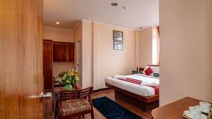 Una camera d'albergo con un letto, una scrivania, una sedia, un tavolino con delle tazze e un vaso con fiori.