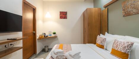 A hotel room with a bed, a TV, a shelf with toiletries, and a painting on the wall.