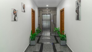 En moderne indretning i en gang med elevator i midten, plantekasser og kunst på væggene.
