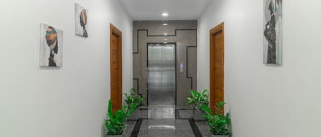 Un pasillo de diseño moderno con un ascensor central, plantas en macetas y obras de arte en las paredes.