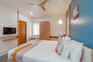 A hotel room with a bed, a TV, a wardrobe, a desk with a lamp, and a painting on the wall.