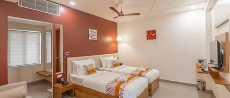 A modern hotel room with two beds, a sofa, a TV, and a small kitchenette.