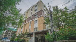 Et fleretagers hotel med facade af mursten, en overdækket indgang og en parkeringsplads med motorcykler.