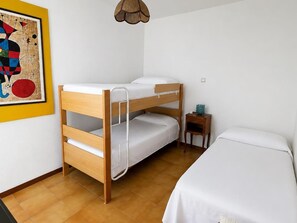 Une chambre avec un lit superposé, une petite table de chevet et un tableau encadré accroché au mur.