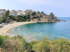 A coastal view with a beach, clear water, and buildings on a hillside.