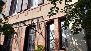 Un bâtiment en briques avec une porte et des fenêtres noires, entouré de verdure.