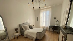 Une chambre à coucher comprenant un lit, une table de chevet, une chaise, un bureau et un miroir.