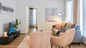 A modern living room with a grey sofa, two pink armchairs, a TV on a black stand, and a painting on the wall.