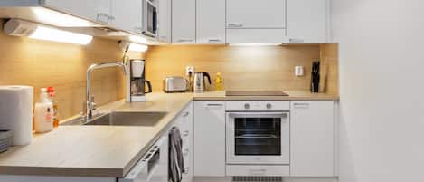 A compact kitchen with white cabinets, a built-in oven, a coffee maker, and a toaster.