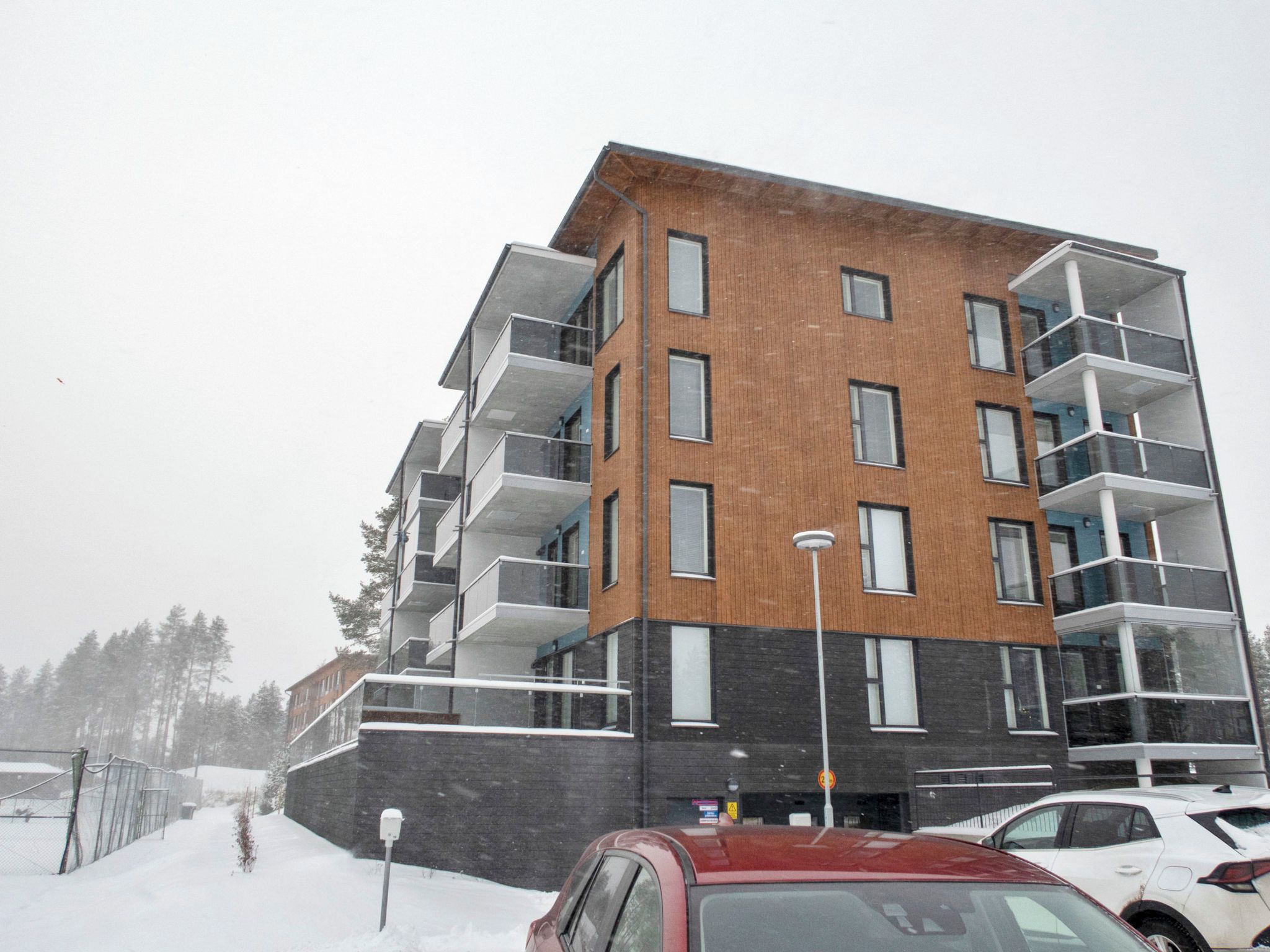 En flereetagers boligbygning med altaner, en murstensfacade og en parkeringsplads med biler.