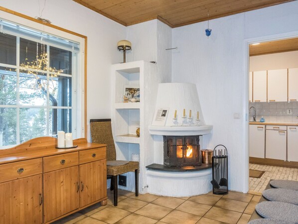 A cozy room with a fireplace, wooden furniture, and a view of a forest through a large window.